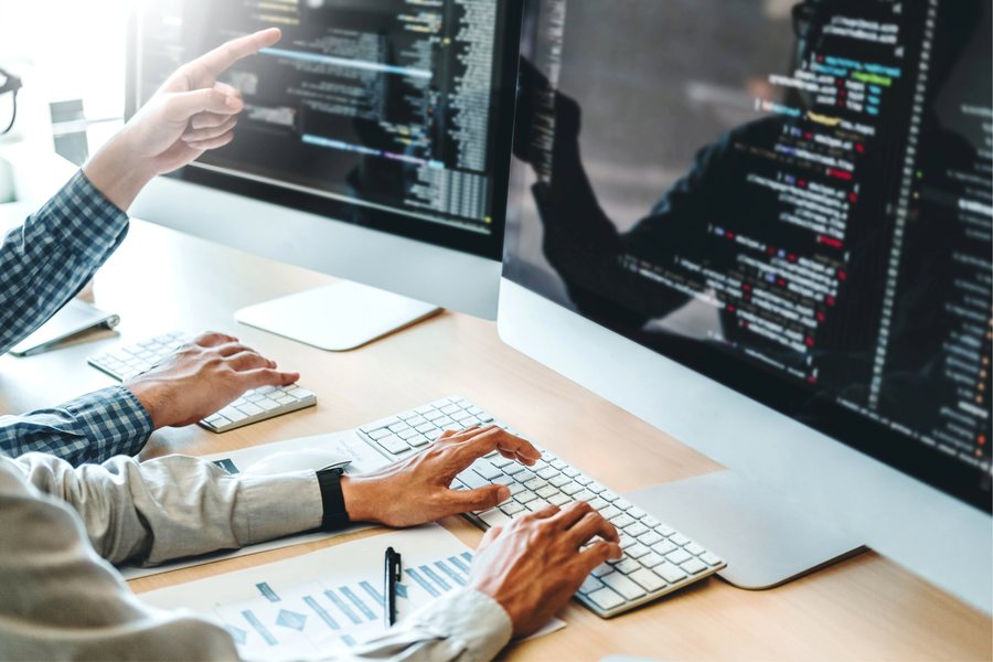 Deux développeurs devant un écran de code, l'un désignant une portion à l'autre